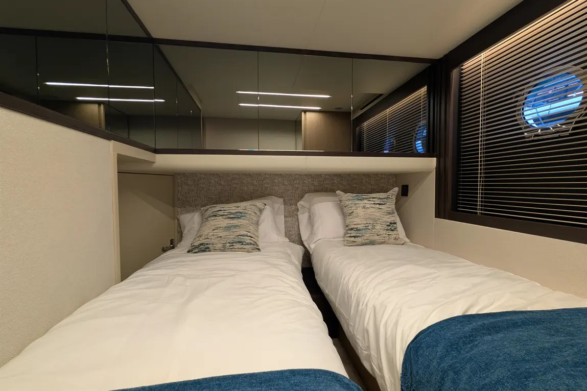 Modern twin bedroom with white bedding, blue accents, and decorative cushions, featuring round windows and mirrors.